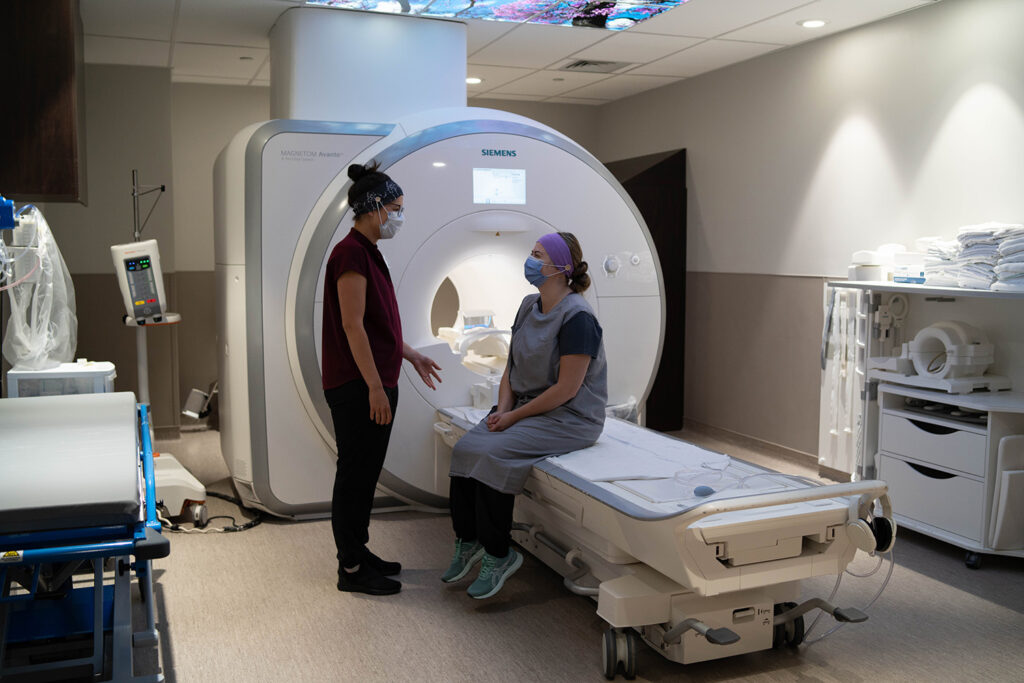 A nurse talks to a patient sitting on the MRI seat